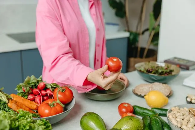 Pessoa próxima à mesa cheia de alimentos saudáveis, como tomates, cenouras e verduras